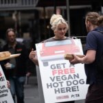 Stefania wears a sign reading - get a free vegan hot dog here!