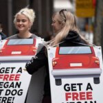 Stefania and Stace wear signs reading: Free Hot Dogs from Cars and Get a Free Vegan Hot Dog Here