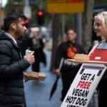 PETA activists wearing sandwich boards hand out hot dog to person on the street