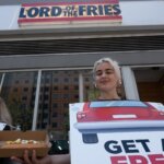 PETA activists wearing sandwich boards hand out hot dog to person on the street with "Lord of the Fries" sign in background