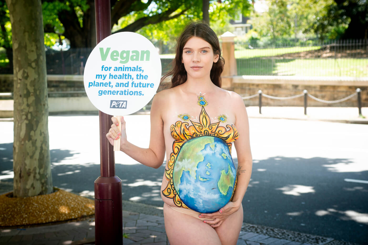 Eliza stands with a sign reading: "Vegan for animals, my health, the planet, and future generations."