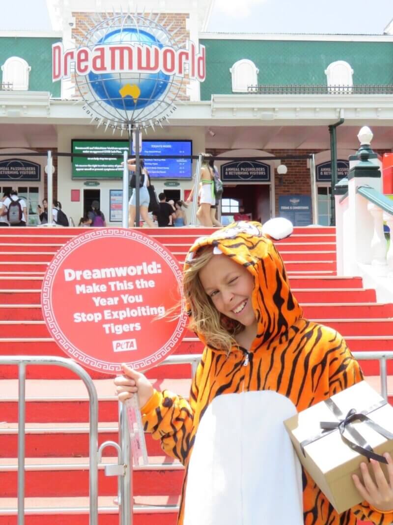 A child dressed in a tiger onesie outside Dreamworld with a sign reading: "Dreamworld: Make This The Year You Stop Exploiting Tigers".