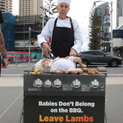 A person wearing a chef's hat and apron pretends to BBQ a doll. Sign reads: "Babies don't belong on the BBQ. Leave lambs alone."