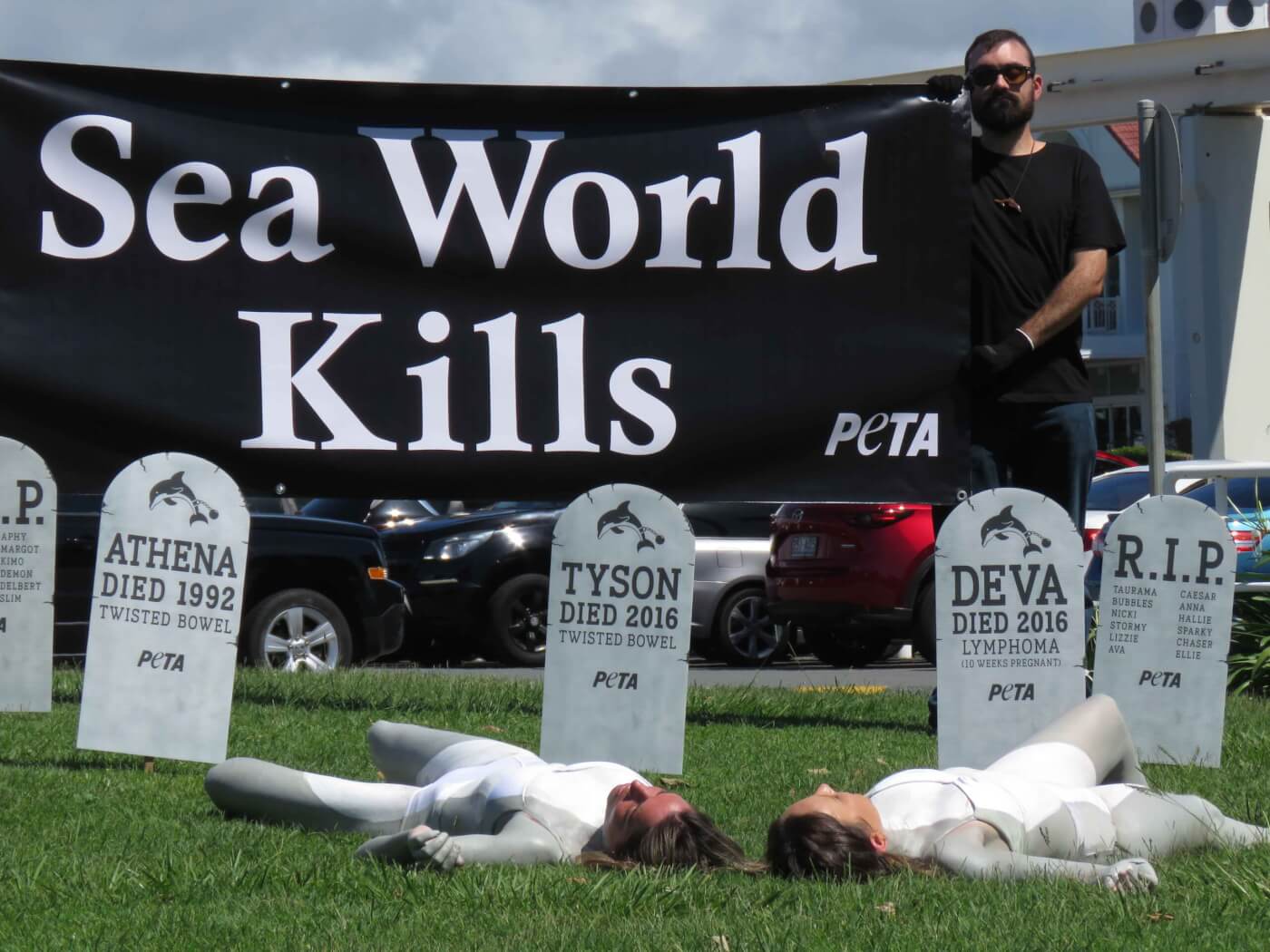 two activists painted grey and white lie under a banner which reads "Se World Kills"