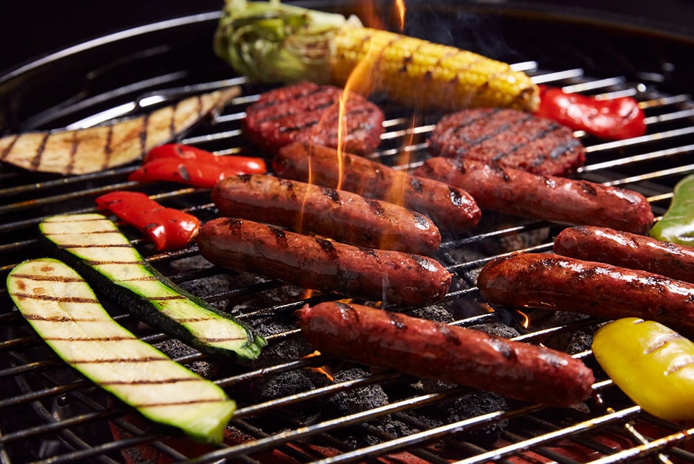 A photo of a vegan BBQ with sausages, burger patties and vegetables.