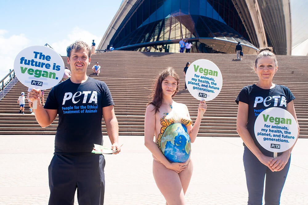 three PETA activists holding signs saying "The Future is Vegan" and "Vegan for animals, my health, the environment, and future generations."