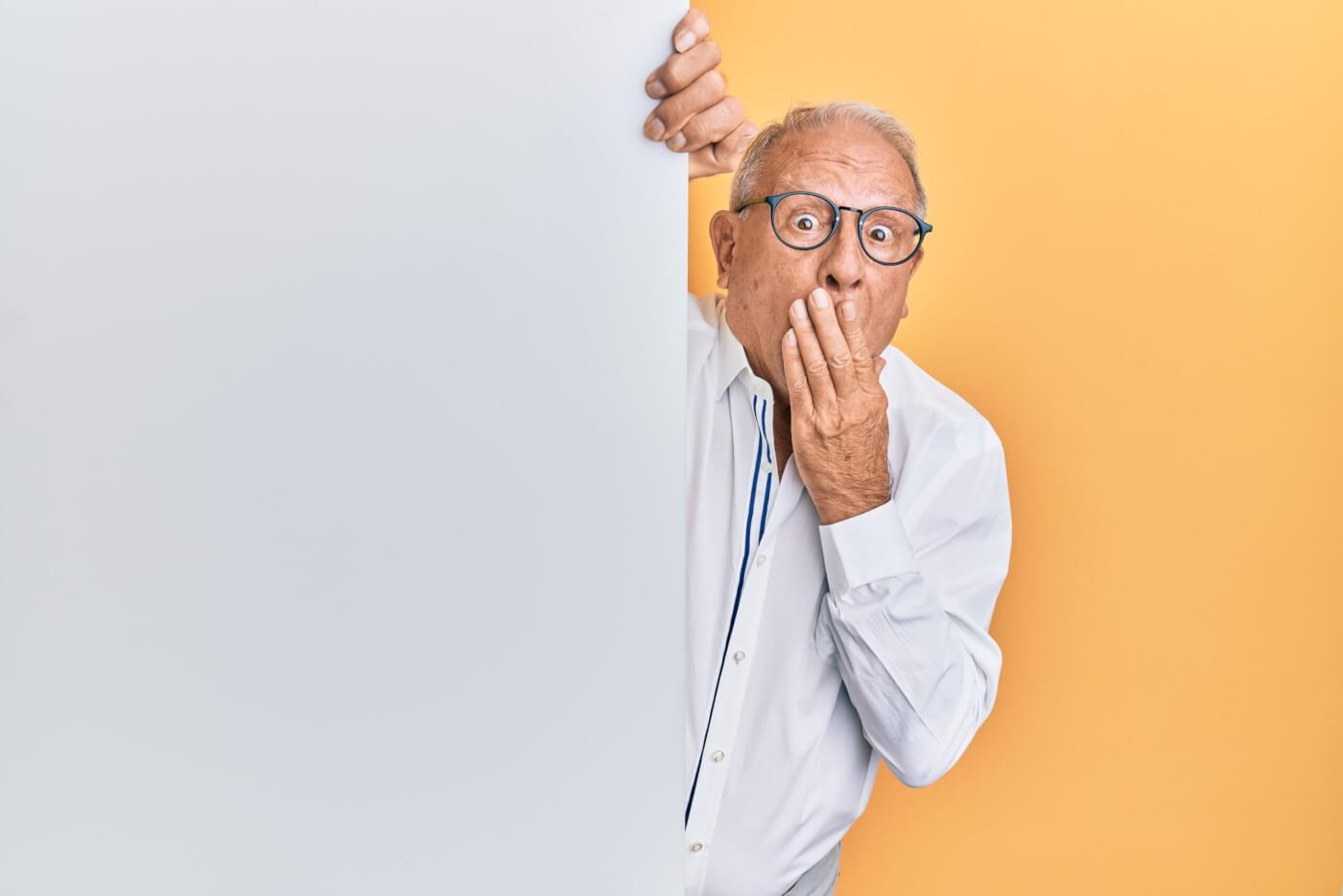 man with grey hair and glasses has hand over mouth