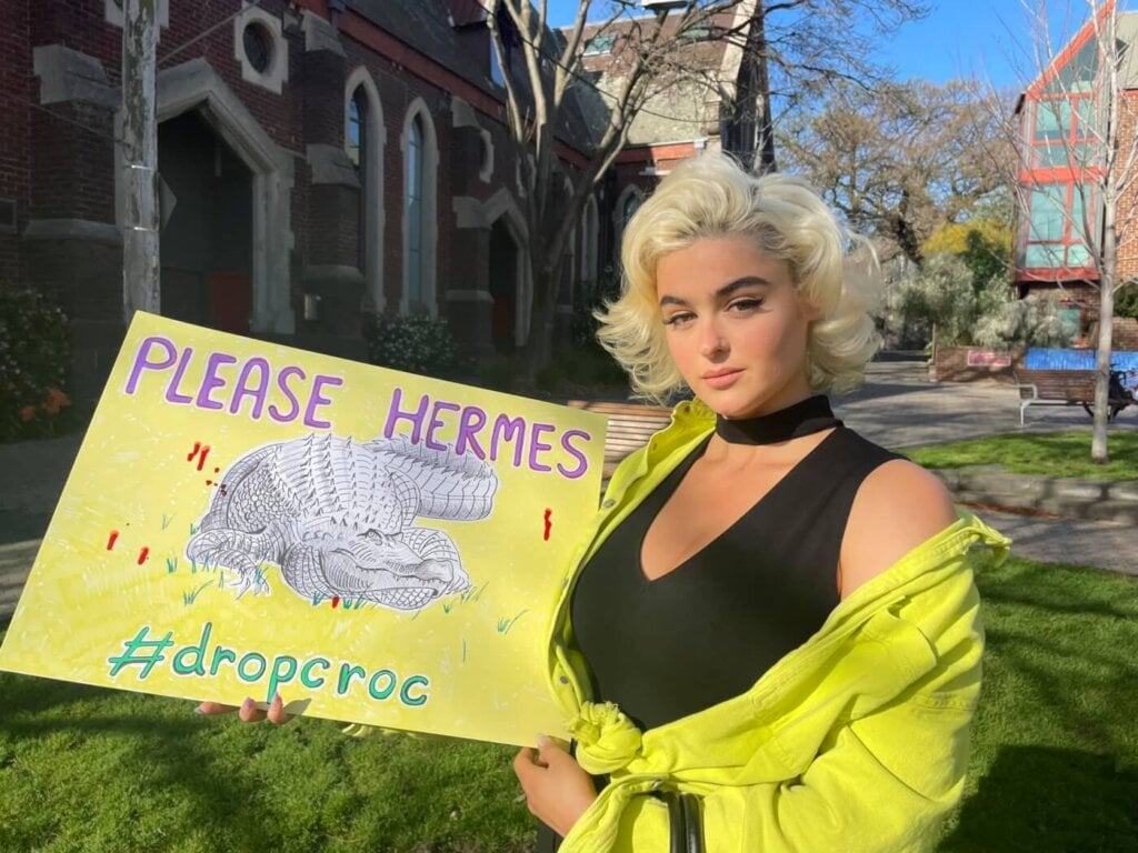Stefania holds a sign asking Hermes to drop croc.